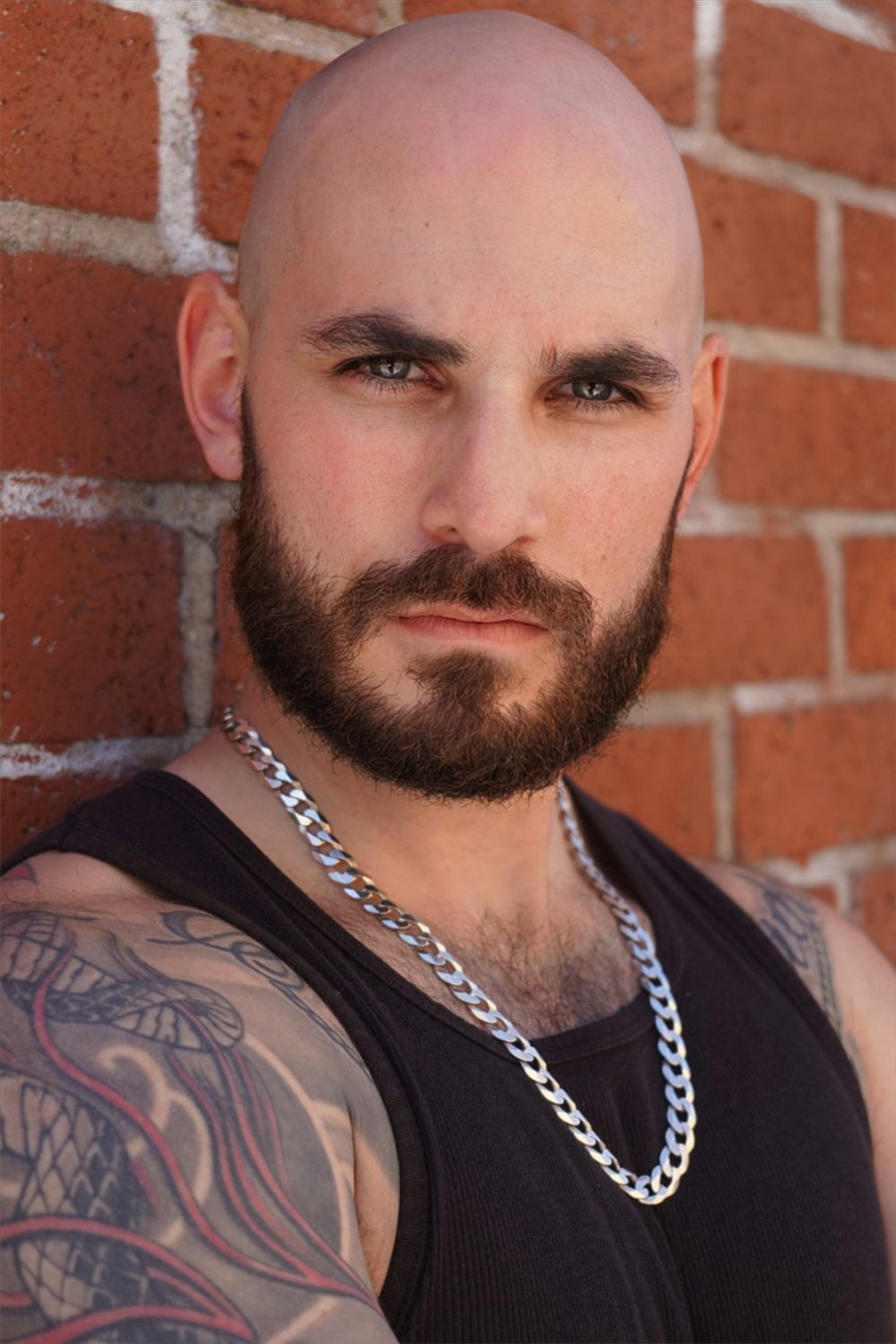 Sirko in a black tank top and chain against a brick wall